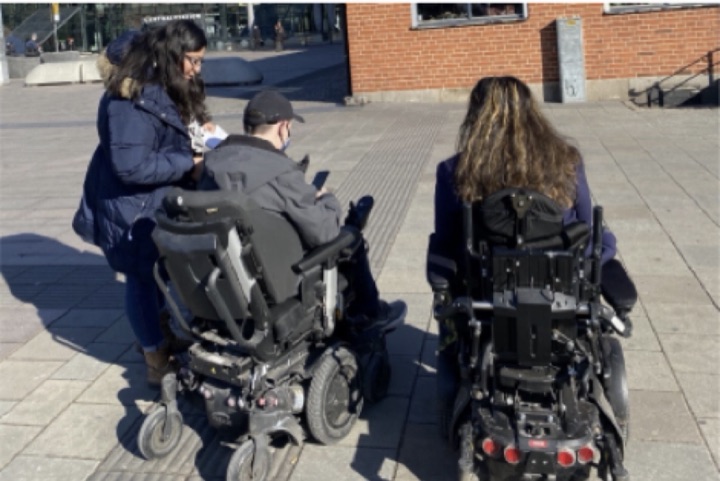 Two wheelchair users talking with a researcher in a town square