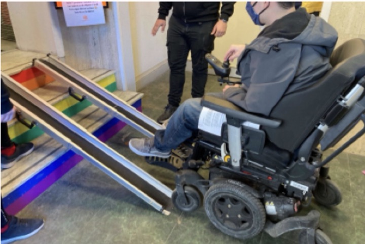 A wheelchair user going down a portable ramp over stairs