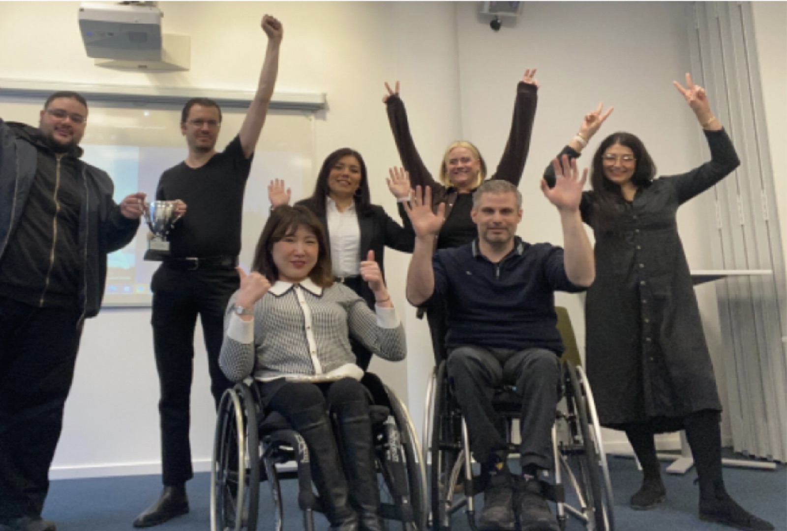 Consuelo celebrating with her team, two of them in wheelchairs, holding a trophy